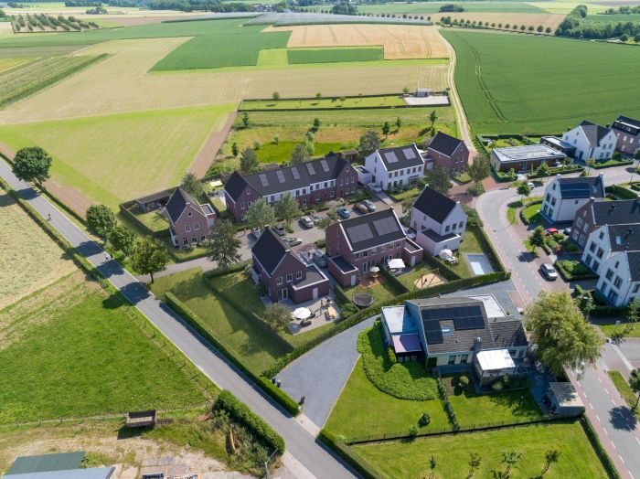 Luchtfoto van het nieuwbouwproject De Bloesemgaard in Margraten, omringd door groene velden en boomgaarden, met duurzaam gebouwde woningen en een rustige woonomgeving.