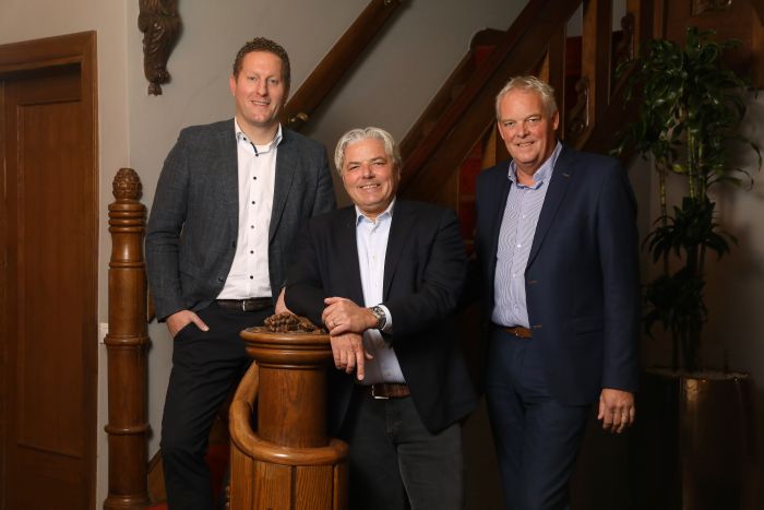 Drie zakenmannen poseren in formele kleding bij houten trap in klassieke interieursetting, portretfoto