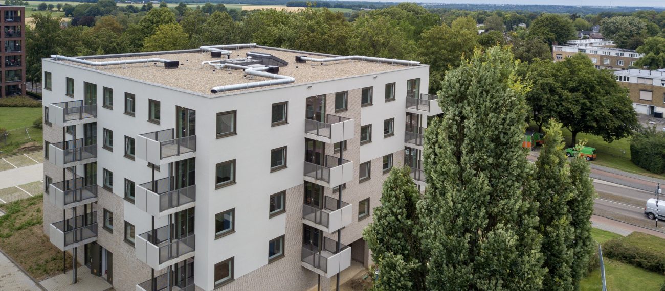 Nieuw appartementengebouw met balkons, omringd door groen.