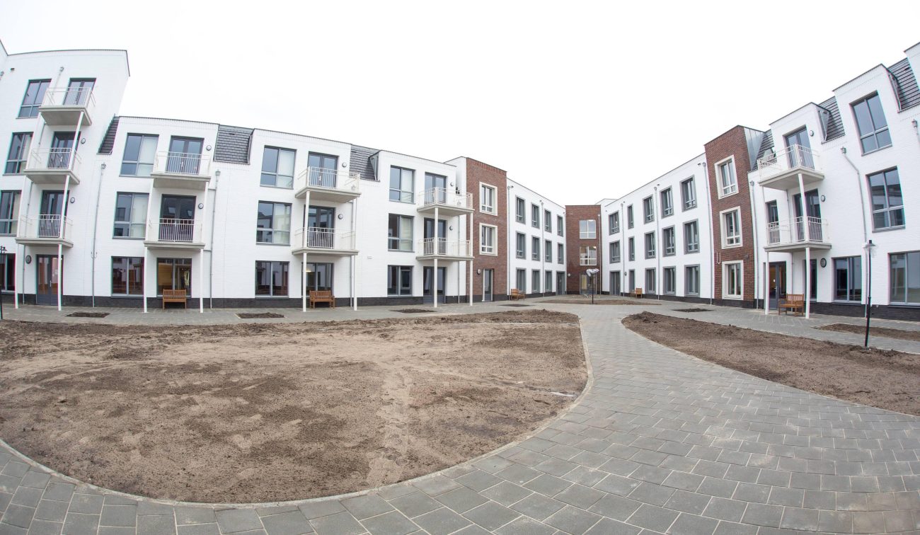 Hof te Berkel Horst – U-vormige binnentuin met slingerpad, zandvakken in aanleg en appartementengevels in wit/rood baksteen met balkons