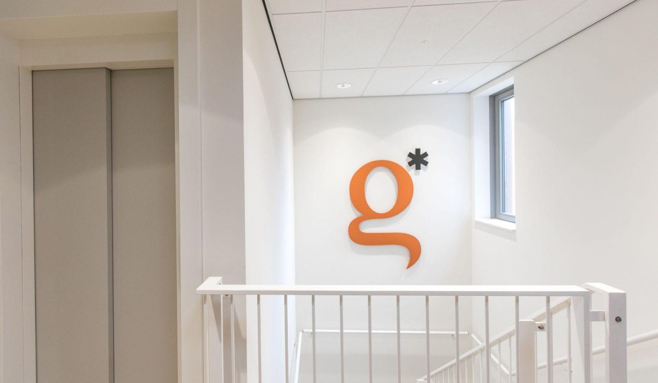 Modern trappenhuis in het nieuwbouwproject van het GZC en de zorgwoningen, met een oranje logo op de muur en natuurlijke lichtinval.