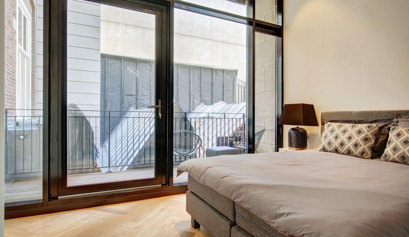 Slaapruimte Oudezijds Voorburgwal: warme visgraatvloer, glazen schuifdeur en uitzicht op patio/balkon