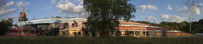 Panorama Ronald McDonald Kindervallei Valkenburg met goudkleurige ui-koepel, golvend blauw dak en kleurrijke organische gevel.