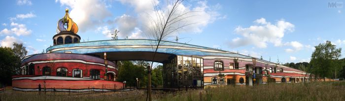 Panoramafoto van de Ronald McDonald Kindervallei in Valkenburg: kleurrige Hundertwasser-architectuur met ronde toren, goudkleurige koepel en brede blauwe boog.