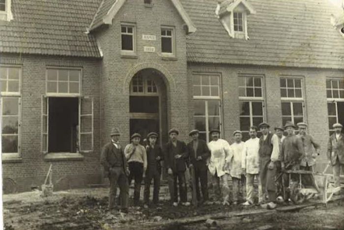 Groep arbeiders poseert voor nieuw bakstenen gebouw tijdens bouwproject, historische foto uit vroege 20e eeuw