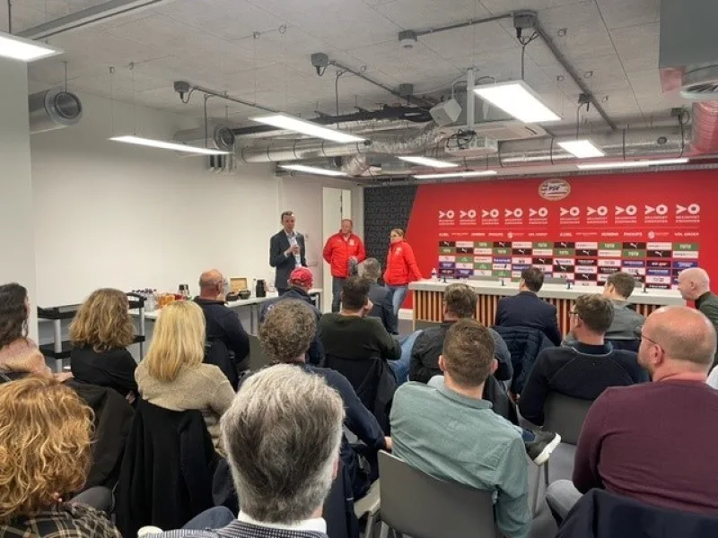 Presentatie voor zittend publiek in vergaderruimte met sponsorwand