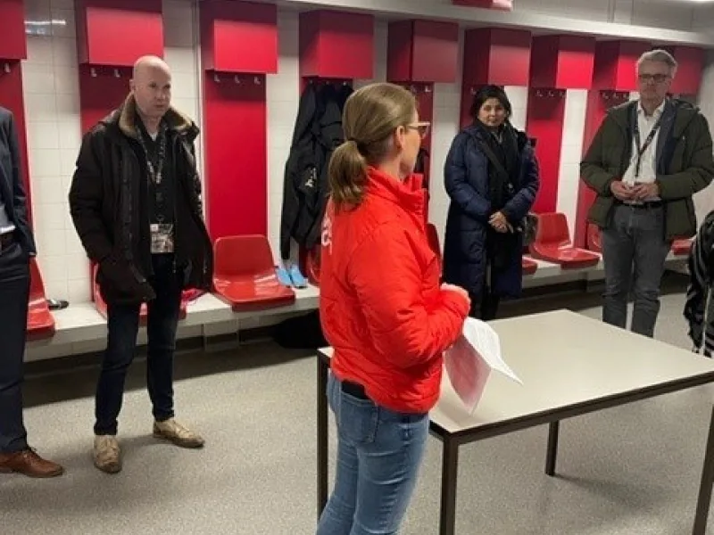 Rondleiding door kleedkamer met rode zitplaatsen en groep bezoekers