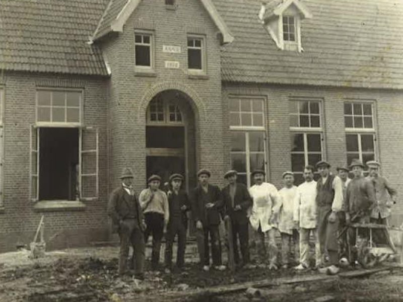 Groep arbeiders poseert voor nieuw bakstenen gebouw tijdens bouwproject, historische foto uit vroege 20e eeuw