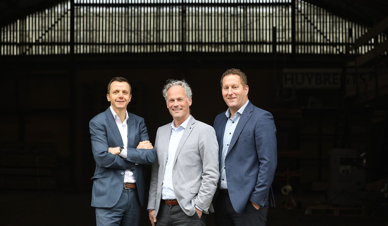 Drie zakenmannen poseren in pak voor industriële loodsopening, moderne zakelijke portretfoto