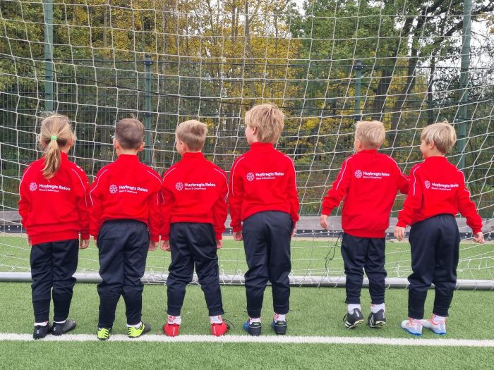 Een team van 6 kinderen poseren op de doellijn met rode trainingsjacks