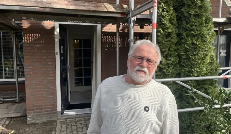 Man staat voor bakstenen woning met steigers rond de gevel