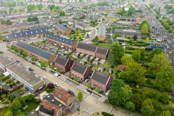 Luchtfoto van een woonwijk in Valkenswaard met in het midden een 3D-impressie van nieuwbouwproject Molensteen: drie bakstenen huizen met donkere zadeldaken en zonnepanelen, tuinen en parkeerplaatsen; op de achtergrond bestaande rijwoningen en veel groen.