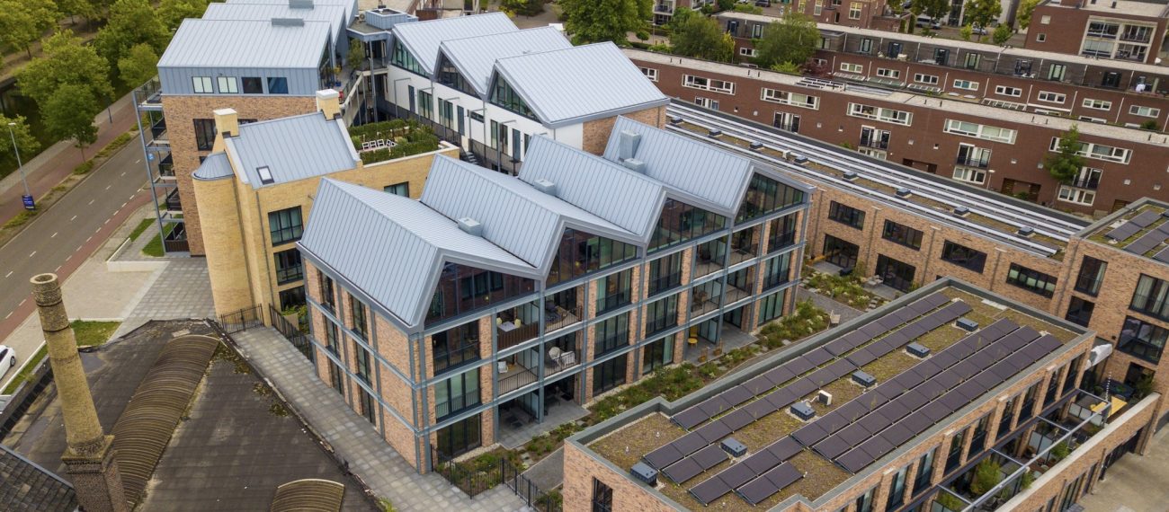 Luchtfoto van modern appartementengebouw met grote ramen, zadeldaken en zonnepanelen op het dak.