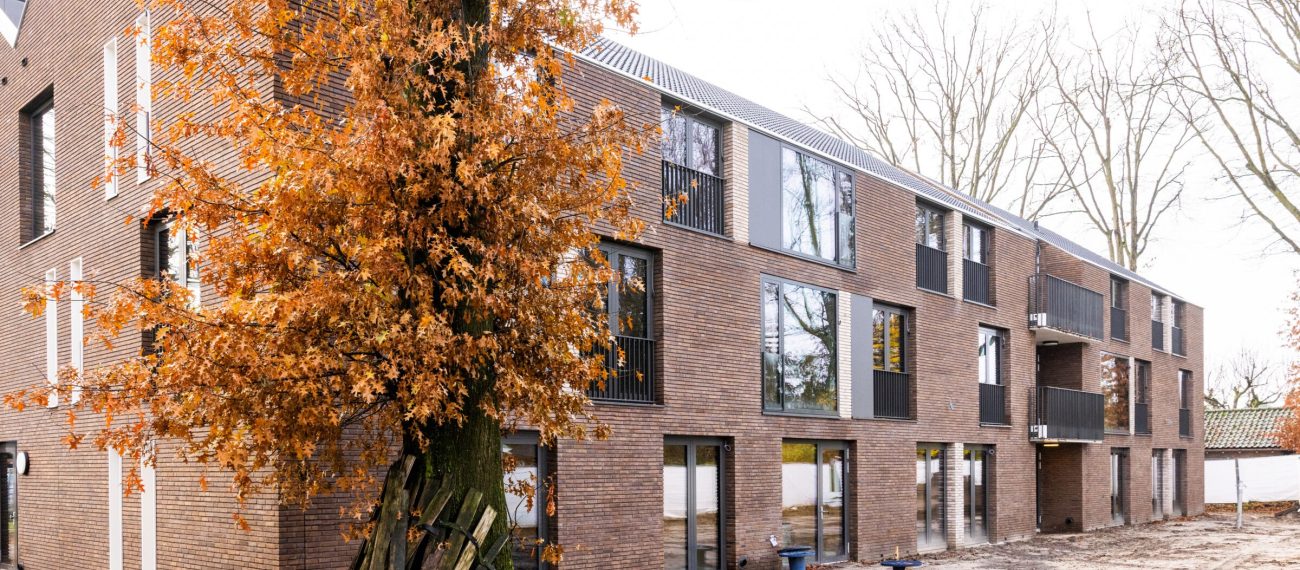 Nieuwbouw van woonzorgcomplex Pontenage in Gemert, een modern bakstenen gebouw met grote ramen en balkons, omgeven door bomen met herfstbladeren