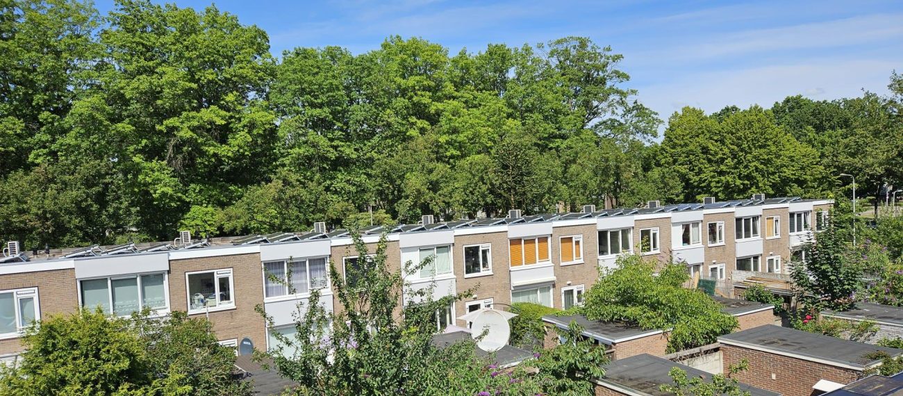 Bovenaanzicht van rijwoningen in de Staatsliedenbuurt Tilburg met zonnepanelen op de daken, omringd door veel groen en bomen.