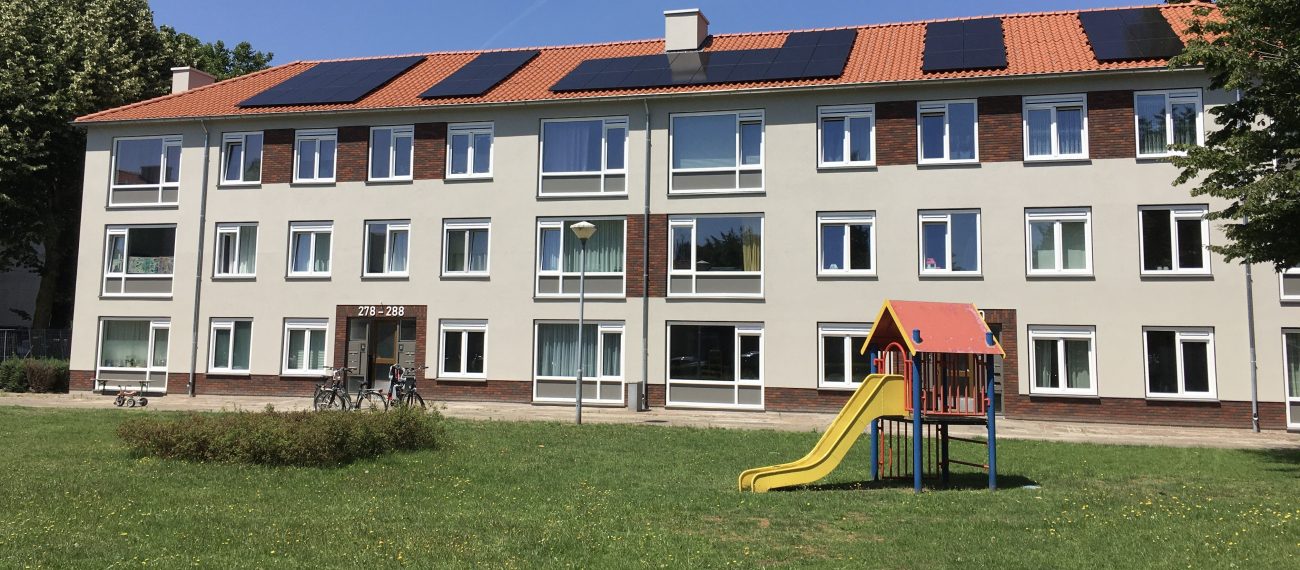 Appartementengebouw met gekleurde gevel en zonnepanelen, met een speeltuin op het grasveld ervoor.