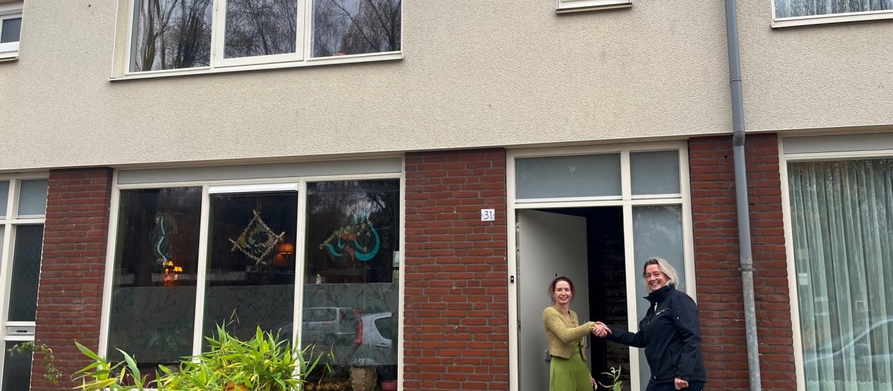 Bewoners staan bij de voordeur van een gerenoveerde woning in een rij huizen.