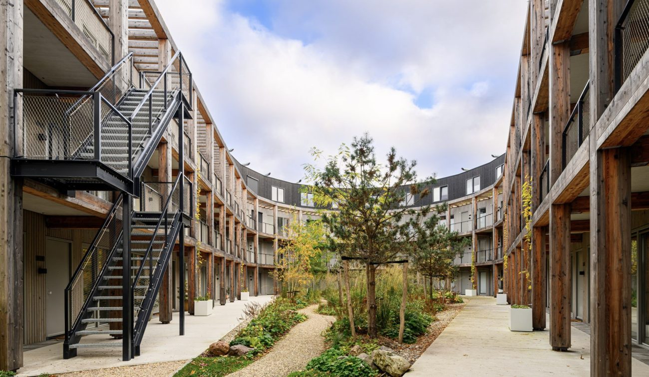 Nieuwbouw ROOT Eindhoven – duurzaam binnenhof met houten gevels, galerijen en groene natuurinclusieve tuin.