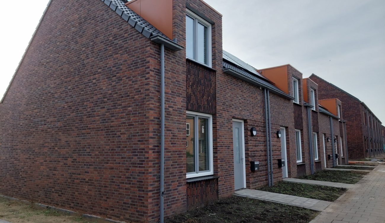 Nieuwbouw Bredeweg Roermond – rijwoningen in rood baksteen met witte kozijnen en oranje dakkapellen, trottoir en voortuinen in aanleg