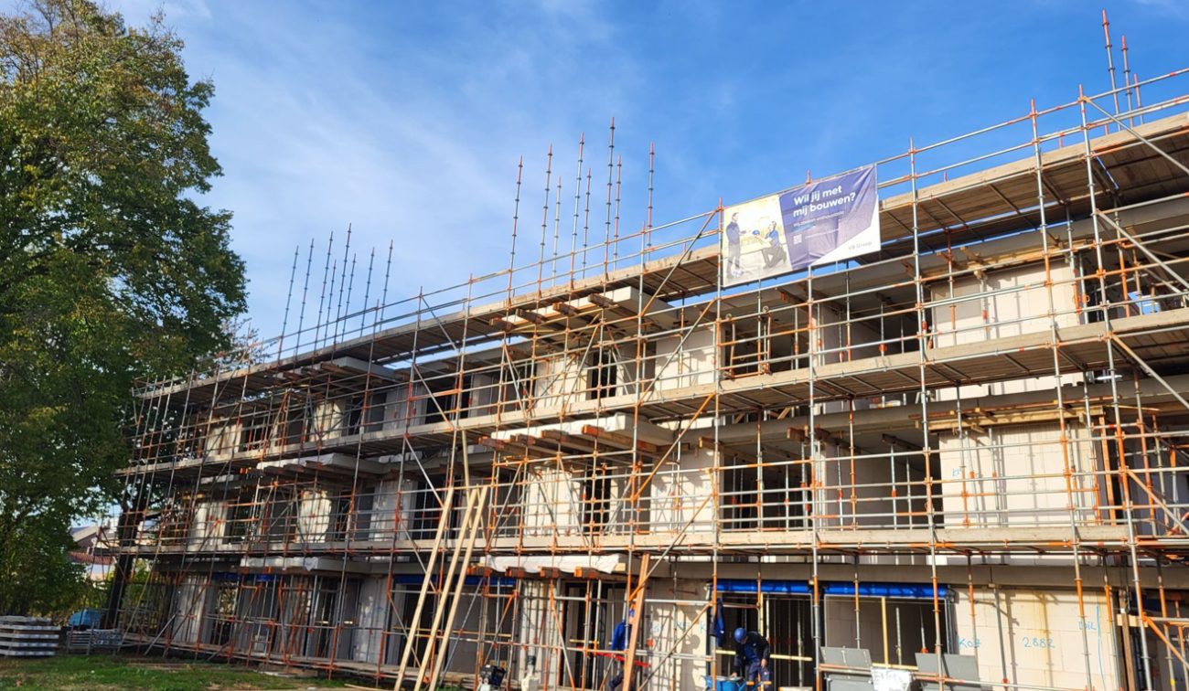 Bouwfase sociale huur Margraten: gevel vol steigers, vaklieden op begane grond