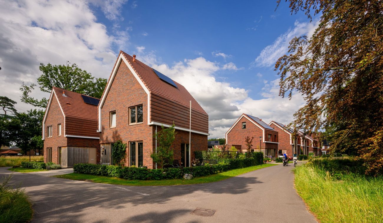 Nieuwbouwwoningen in Kloostervelden in Sterksel met rode baksteen, zonnepanelen en een groene straat met bewoners op de fiets.
