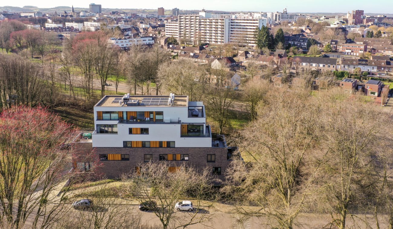 Terrasappartementen met zonnepanelen op dak, omringd door bomen en woonwijk — Gebiedsontwikkeling Parkheuvel Heerlen