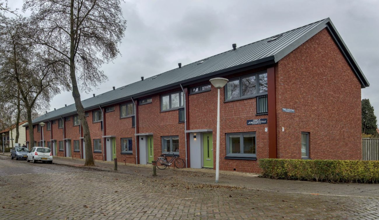 Renovatie (groot onderhoud) NOM van 195 rijwoningen in ’t Ven, Eindhoven – straatbeeld met rode bakstenen gevels, groene voordeuren, nieuw metalen dak, bomen en kasseien, fiets bij de gevel.