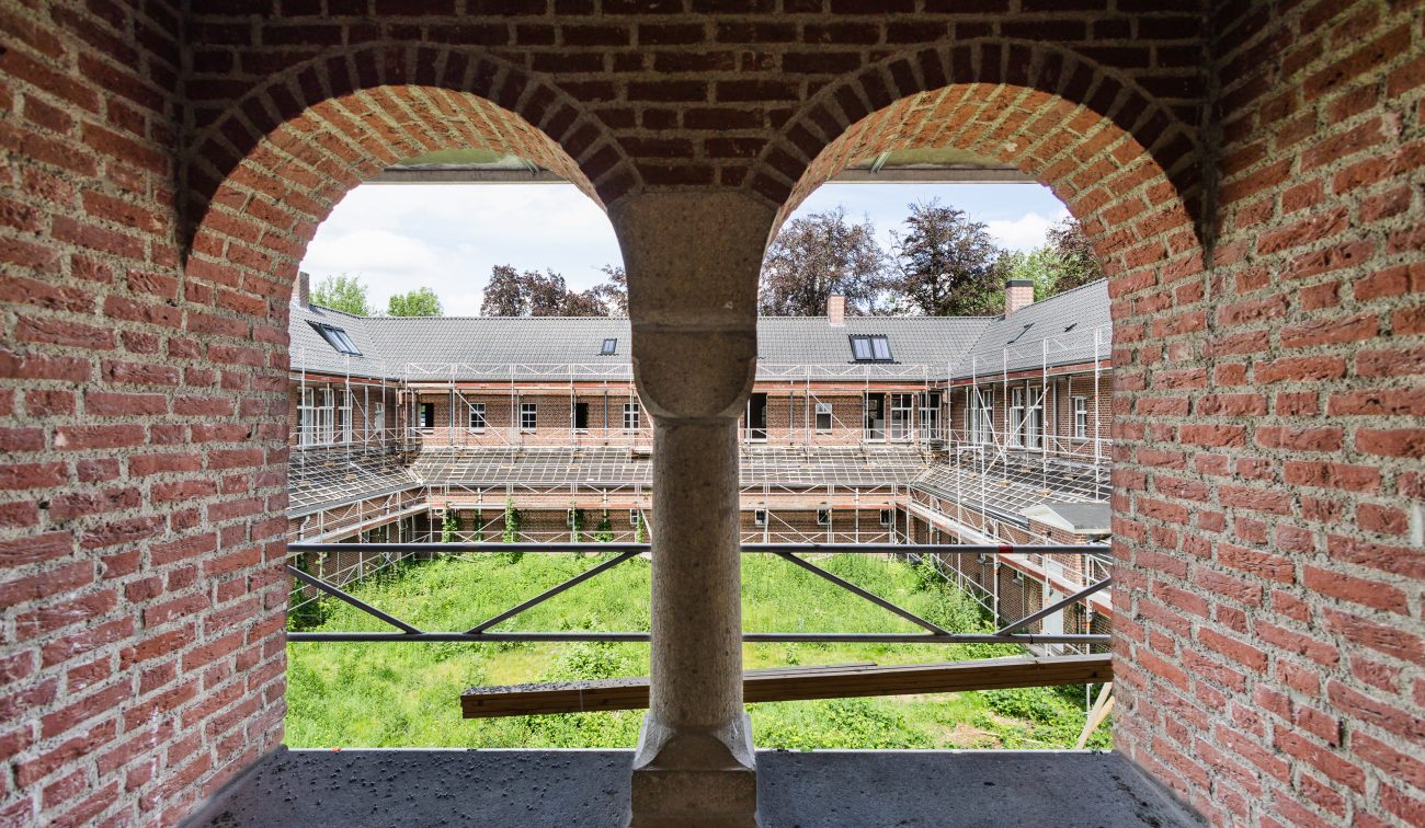 Bakstenen galerij met bogen en uitzicht op steigers rond begroeide binnentuin tijdens renovatie