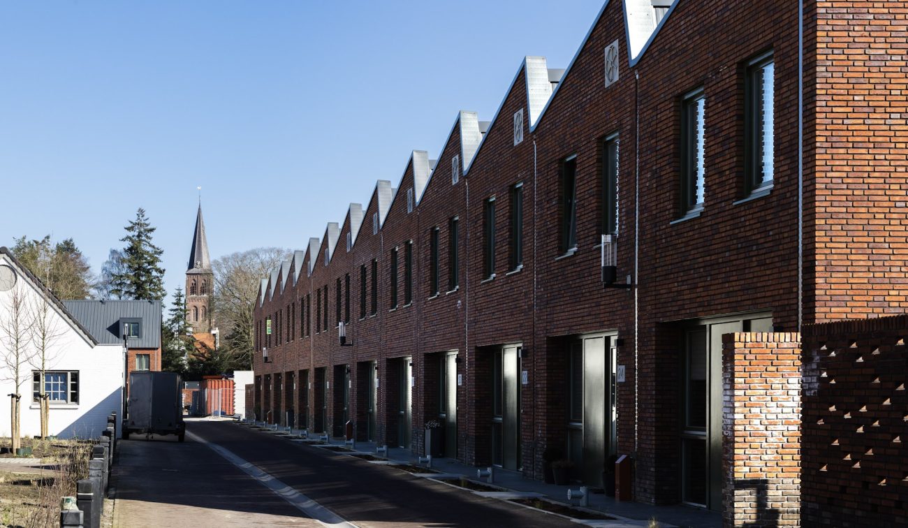 Rijwoningen met bakstenen gevels en hoge daklijnen langs smalle woonstraat in nieuwbouwwijk