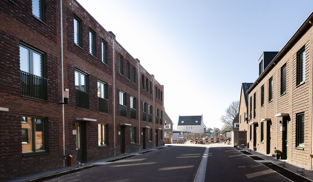 Nieuwbouwwoningen met bakstenen gevels langs brede woonstraat tussen aaneengesloten woonblokken