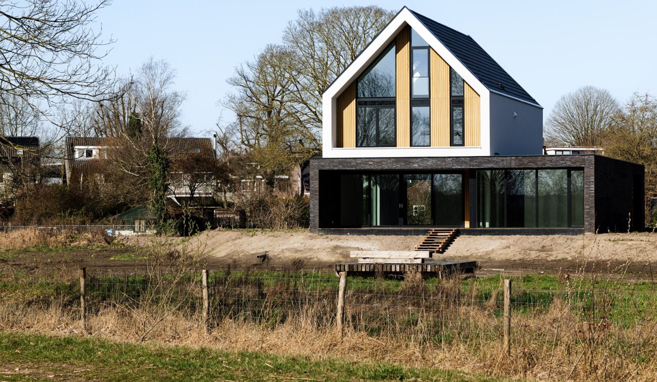 Vrijstaande nieuwbouwwoning met hoge raampartijen en donkere gevel aan groen landschap