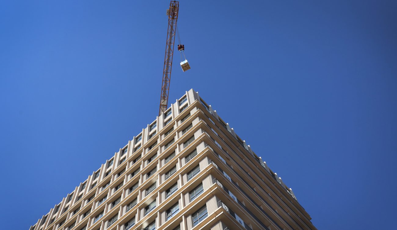 Hoek van goudkleurige woontoren De Bankier met hijskraan en helderblauwe lucht — Nieuwbouw De Bankier Tilburg