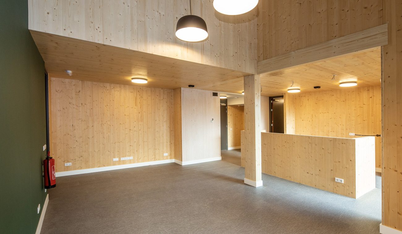 Ruim interieur van het woonzorgcomplex Pontenage in Gemert, met lichte houten wanden en plafonds, moderne verlichting en een open indeling met hoge plafonds.