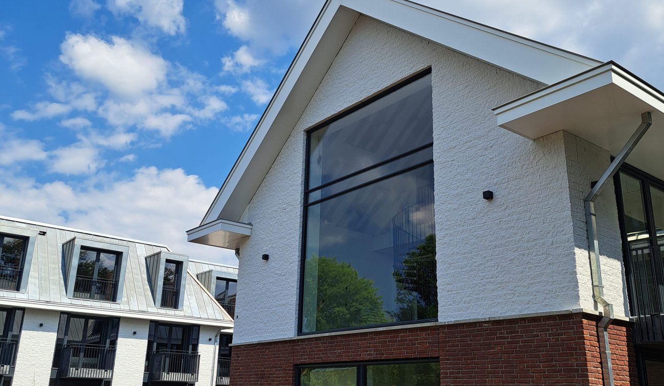 Uitbreiding en renovatie Van der Valk Hotel Wassenaar – paviljoen met witte gevel en bakstenen plint, hoge glazen pui en zinken dakdetails, met binnenhof en aanleg van de tuin op de voorgrond.