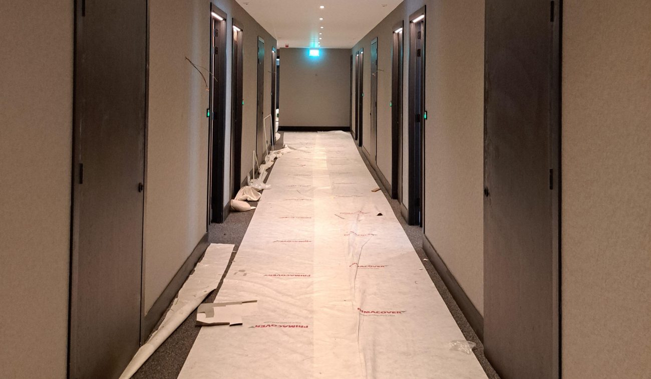 Uitbreiding en renovatie Van der Valk Hotel Wassenaar – hotelgang in afbouw met schilderklare wanden, nieuwe deuren en beschermfolie over de vloer, spotverlichting aan het plafond.