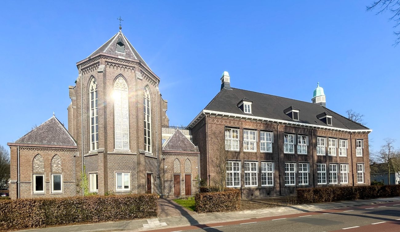 Verbouwing Huize Padua Boekel – straataanzicht van het monumentale complex met kapel en gotische ramen, bakstenen gevels en witte kozijnen onder een heldere blauwe lucht.