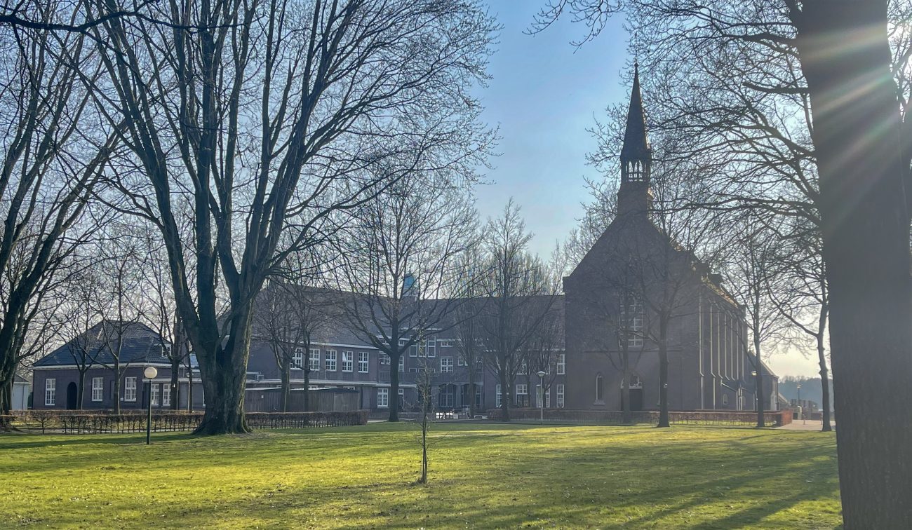 Verbouwing Huize Padua Boekel – zicht vanaf het park op het monumentale complex met kapel en hoge torenspits, omringd door bomen met laag zonlicht.