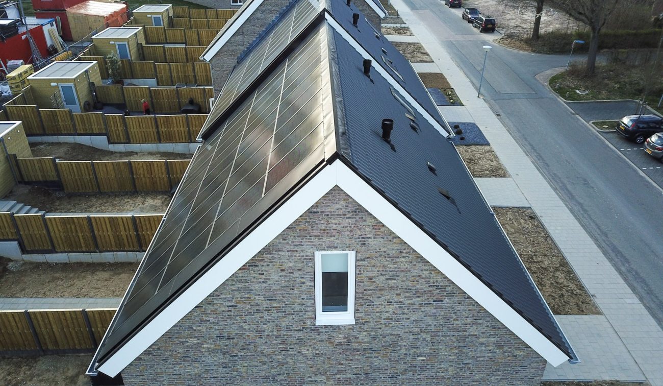Detail luchtfoto rijwoningen Hulsberg met zadeldaken vol geïntegreerde zonnepanelen, zicht op achtertuinen en straat met parkeervakken.