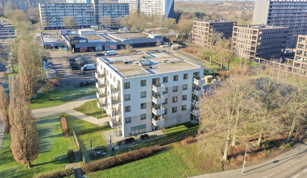 Luchtfoto nieuwbouw Noorderkroon Brunssum – vijflaags appartementengebouw met balkons en plat dak, gelegen naast winkelcentrum en hoogbouw in groen stadsdeel