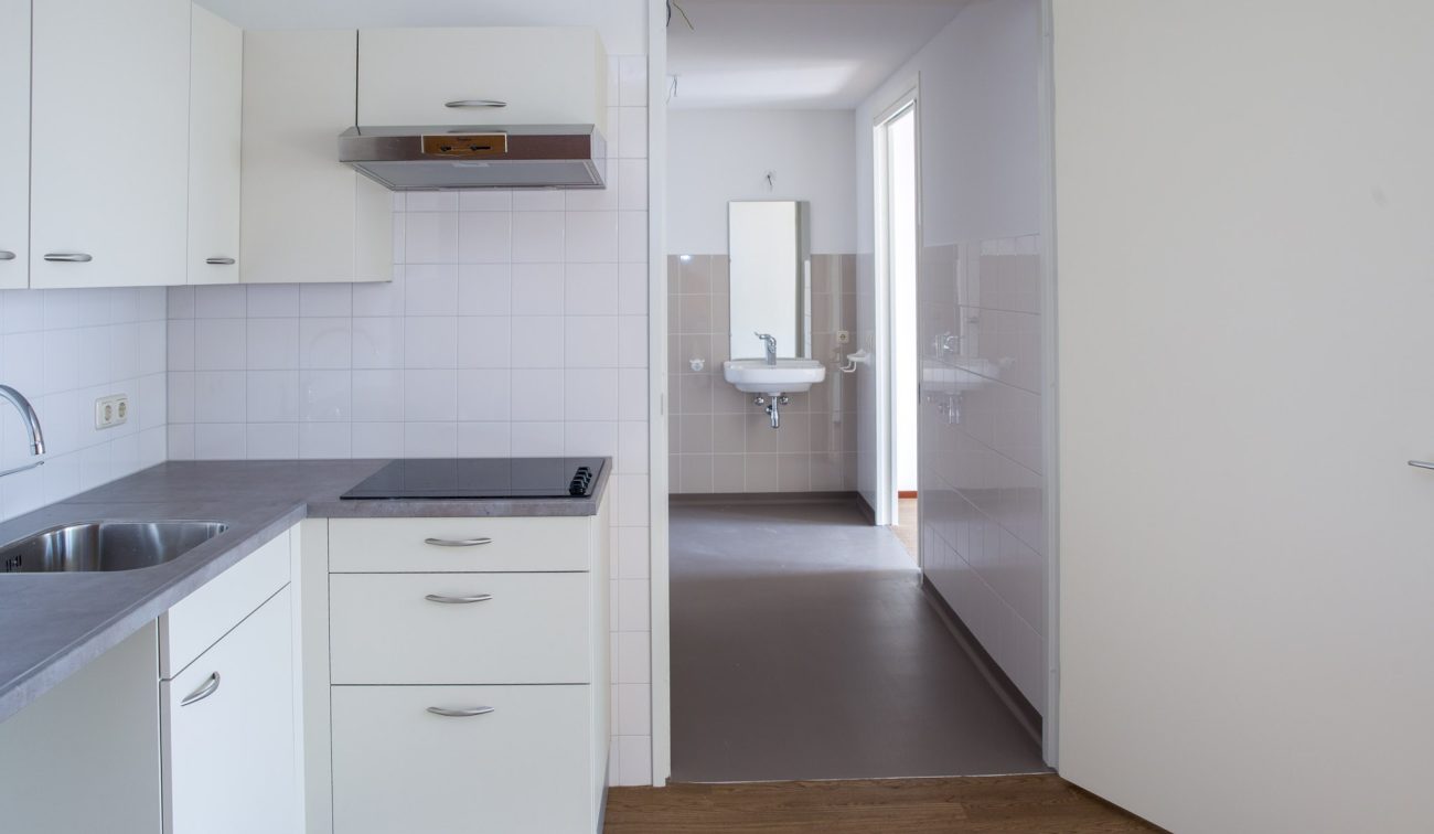 Keuken in zorgwoning met inductiekookplaat, witte kasten en zicht op badkamer.