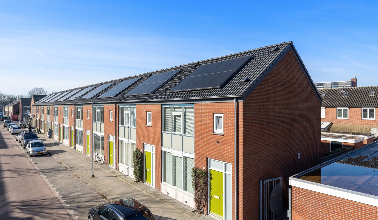 Wandelbos Tilburg verduurzaming: rijwoningen met zonnepanelen, rode baksteen en groene deuren. strak