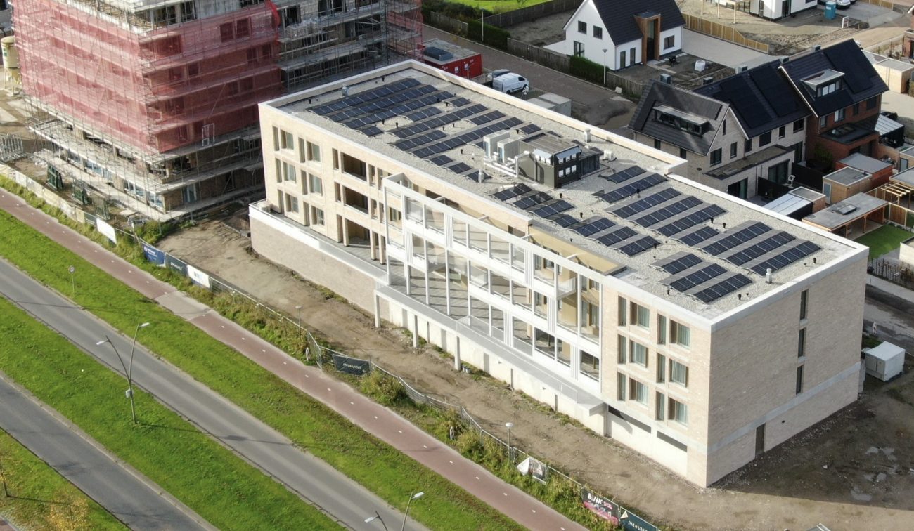 Nieuwbouw De Baron Bergen op Zoom: licht baksteen woonblok met zonnepanelen op dak, luchtfoto zonnig