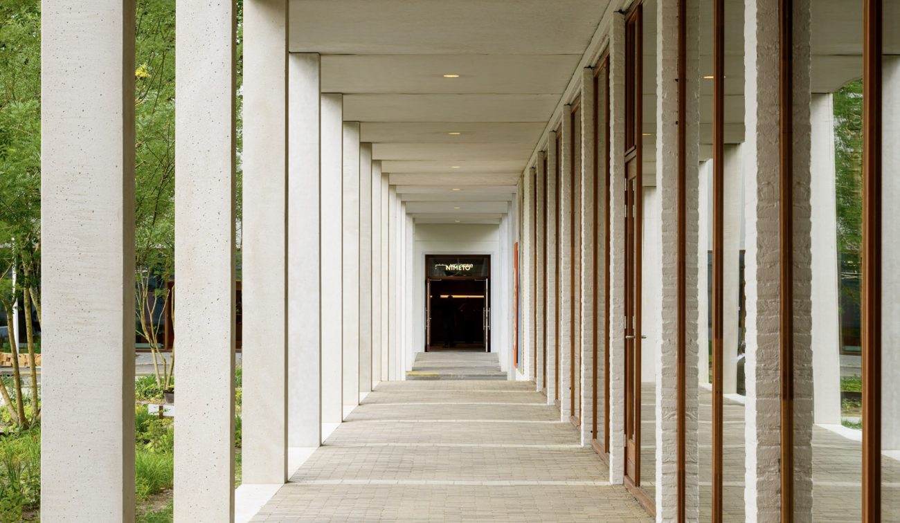 Overdekte galerij Nimeto Utrecht met houten kozijnen, witte baksteen en zicht op groene tuin.