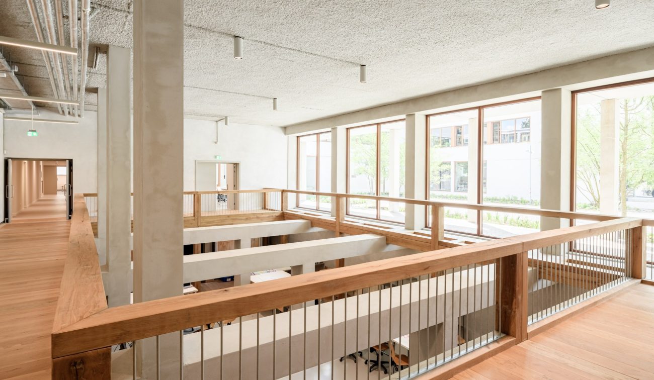 Interieur Nimeto: betonnen kolommen, glasstroken en warm hout, met open vide naar werkruimte.