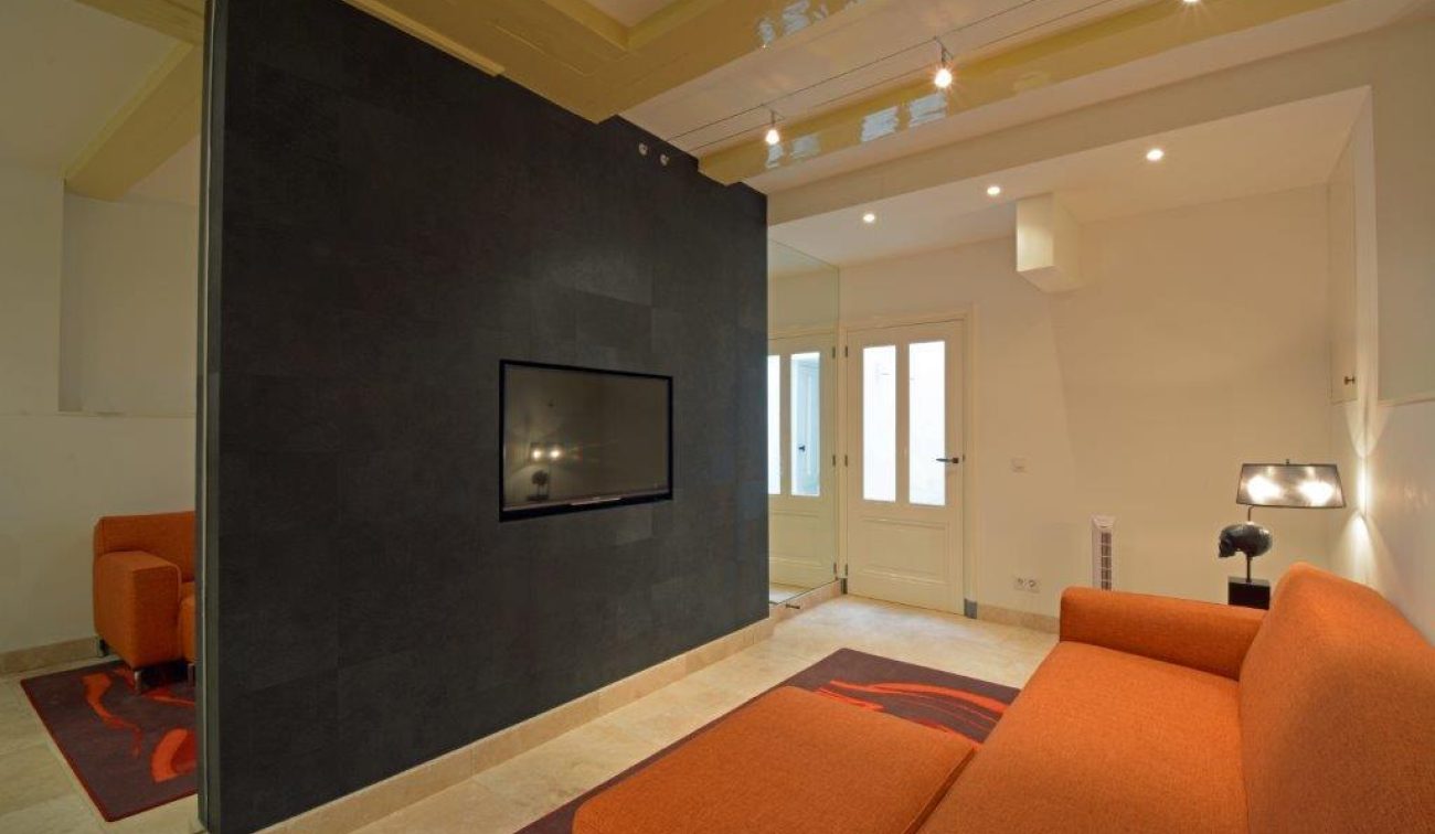 Renovatie Egelantiersgracht: compact zitgedeelte met oranje sofa, tv in zwarte wand en inbouwspots