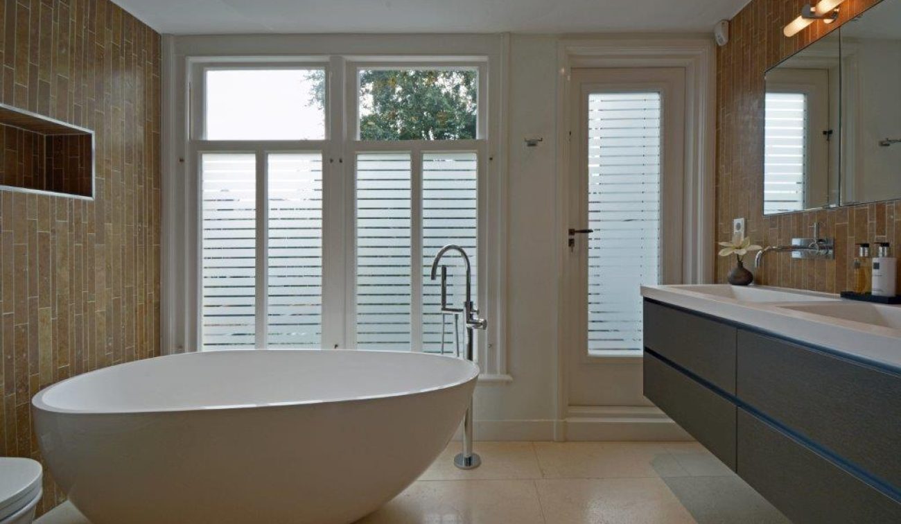 Renovatie Egelantiersgracht: serene badkamer met losstaand bad, jaloezieglas en strak hangmeubel