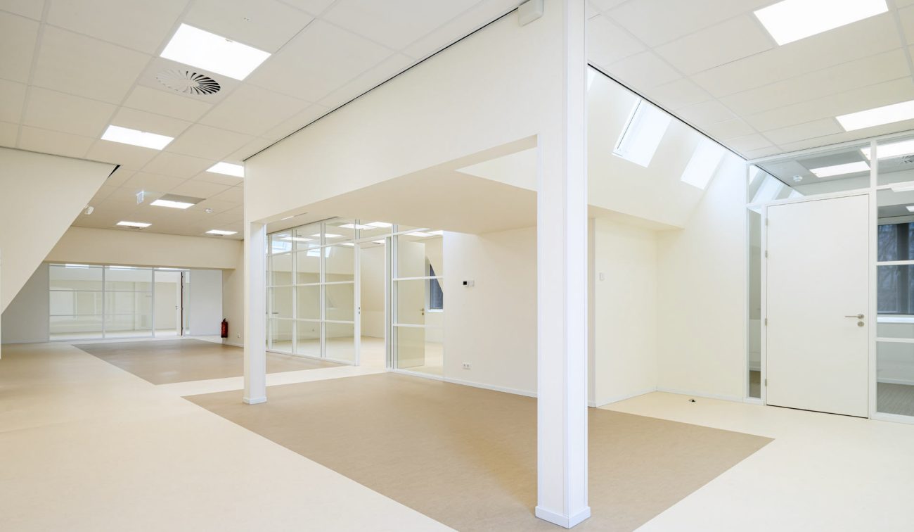 Renovatie Kindcentrum LEF Utrecht – open leerplein met glazen scheidingswanden en veel daglicht via daklichten; rustige materialen en vloerzones creëren overzicht en flexibiliteit.