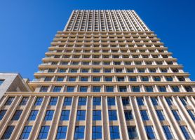 Ontwikkeling De Bankier Tilburg – close-up omhoogkijkend perspectief van de toren met ritmische geveldetaillering en grote raamvlakken tegen een helderblauwe lucht.