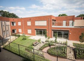 Tuin van het nieuwbouwproject met het GZC en de zorgwoningen, met groene beplanting en buitenruimte voor bewoners.