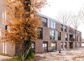 Nieuwbouw van woonzorgcomplex Pontenage in Gemert, een modern bakstenen gebouw met grote ramen en balkons, omgeven door bomen met herfstbladeren